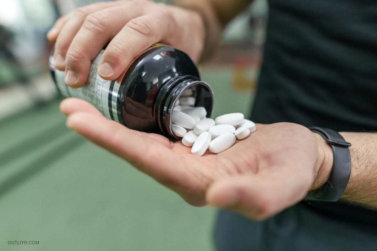 Closeup of sporty muscular man arms showing sports and fitness supplements, capsules, pills