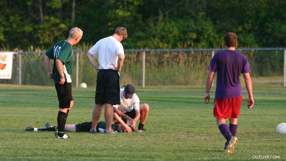 Soccer players gathering around a concussed player on the ground