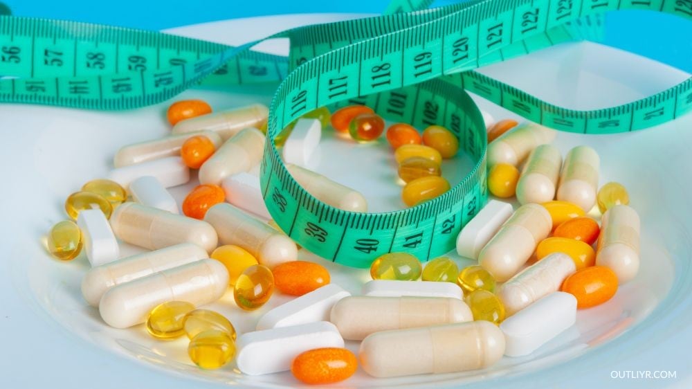 A measuring tape over some pills and vitamins in a plate